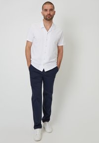 Camisa blanca de manga corta con botones y cuello, combinada con pantalones azul marino y zapatillas blancas. Diseño y tela casuales y limpios.