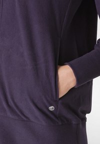 Felpa viola con una texture liscia, maniche raglan, tasche laterali e polsini a costine. Presenta un piccolo logo di colore contrastante.