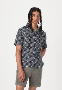 Chemise à manches courtes avec une base navy et un motif floral blanc, fabriquée en tissu léger. Associée à un short en velours côtelé clair.