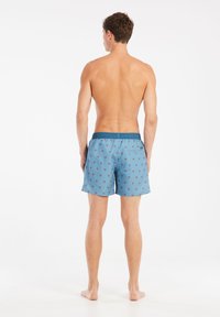 Mėlynos maudymosi šortai su raudonu palmės dekoru. Turi elastingą liemenį ir šonines kišenes. Medžiaga atrodo lengva ir pralaidi orui.