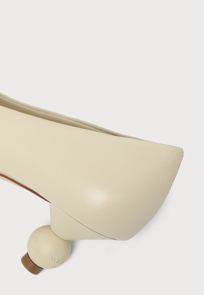 Chaussure femme couleur crème avec un bout carré arrondi et un talon unique en forme de boule ronde sur fond blanc.