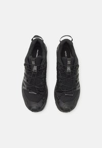 Des chaussures de sport noires avec une tige en maille texturée, des lacets élastiques et un capuchon renforcé. Elles disposent d'une languette au talon pour un enfilage facile.