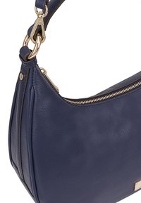 Navy leren schoudertas met een gebogen vorm, gouden hardware en een ritssluiting. Heeft een gestructureerd oppervlak en accentpanelen aan de zijkant.