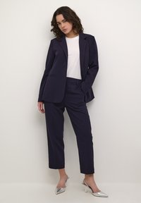 Blazer marine et pantalon court assorti en tissu lisse. Associé à un t-shirt blanc et des escarpins argentés à bout pointu. Design simple, coupe ajustée.