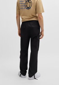 Juodos cargo kelnės su didelėmis šoninėmis kišenėmis, reguliaraus kirpimo ir elegantiško dizaino, derinamos su tan spalvos trumpomis rankovėmis marškinėliais, turinčiais grafiką.