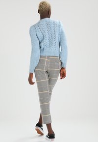 Maglione lavorato a maglia blu chiaro con retro decorato, abbinato a pantaloni a quadri grigi cropped e sneakers nere. Texture e dettagli di design visibili.