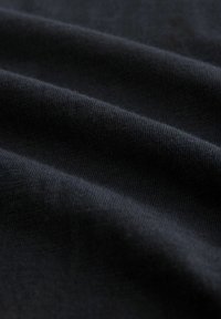 Tissu noir avec une texture douce et lisse, présentant des plis diagonaux et un motif en fine maille. Aucun matériel ou accent notable présent.