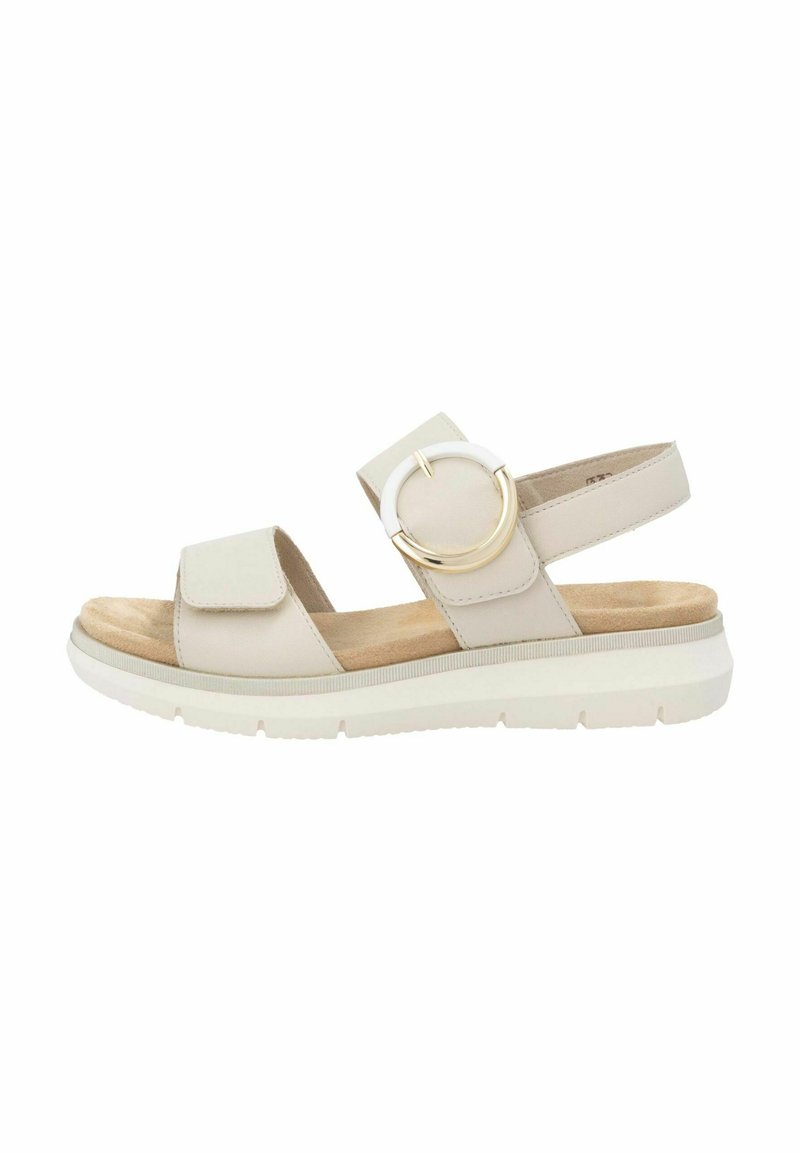 Sandales beiges avec un dessus synthétique lisse, une sangle ajustable, un grand accent métallique circulaire et une semelle intérieure rembourrée sur une semelle blanche.