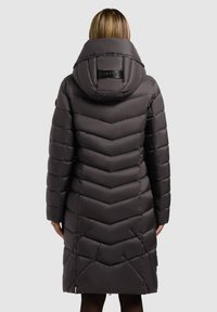 Tmavohnedý páperový kabát s šípovým prešívaním, kapucňou a logom na zadnej strane. Hladký povrch a dizajn po kolená.