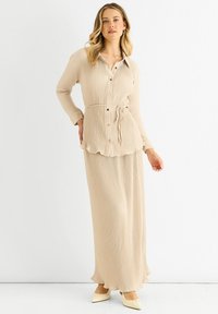 Beige ribbed dress with a collared button-down top, cinched waist, and flowing skirt. Features a scalloped hem and long sleeves.