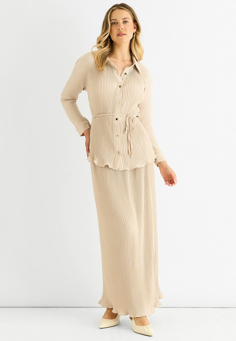 Beige ribbed dress with a collared button-down top, cinched waist, and flowing skirt. Features a scalloped hem and long sleeves.