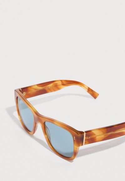 Γυαλιά ηλίου με καφέ-πορτοκαλί σκελετό, μπλε φακούς, τετράγωνο σχήμα και χρυσές λεπτομέρειες στα μπράτσα, με κομψό, γυαλιστερό φινίρισμα.