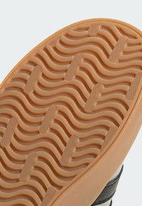 Gumeni potplat cipele s teksturiranim valovitim uzorkom, u narančastoj boji s žlijebovima i izbočinama za bolje prianjanje. Ivice su glatke i zaobljene.