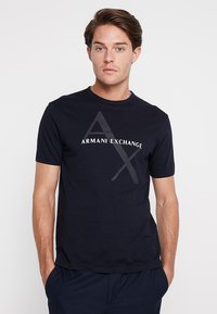 Mørkeblå bomulls t-skjorte med korte ermer, med en kontrasterende grå "Armani Exchange"-logo og geometriske detaljer på forsiden.
