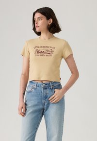 T-shirt beige tagliata con maniche corte e scollatura rotonda. Presenta una stampa grafica rossa con la scritta "LEVI STRAUSS & CO. TWO HORSE BRAND."