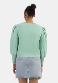 Felpa verde menta con maniche a sbuffo, polsini e orlo a coste, abbinata a una gonna di denim chiaro con orlo sfilacciato.