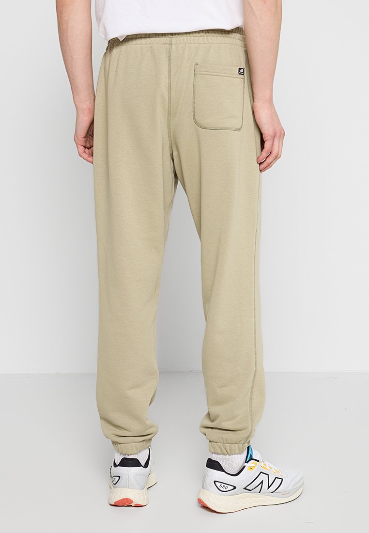Pantalons de survêtement beige clair avec une taille élastique, des poignets élastiques et une poche arrière unique. Fabriqués en matériau doux avec des coutures visibles.