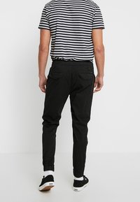 Czarne spodnie dresowe z elastycznym pasem i mankietami, z bocznymi kieszeniami i prostą, gładką teksturą. Noszone z koszulą w paski i trampkami.