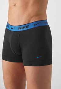Črne Nike bokserice z modrim elastičnim pasom, na katerem je Nike logo. Gladek material, prilegajoča oblika in minimalni detajli šivov.