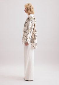 Haut blanc à motif cachemire avec une coupe décontractée et des manches longues, associé à un pantalon blanc à jambes larges. Tissu lisse avec un design fluide.