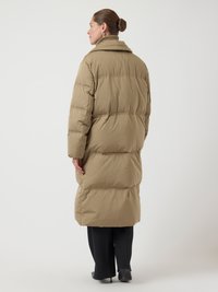 Lungo cappotto puffer beige con colletto alto e dettagli di cucitura orizzontale, caratterizzato da una vestibilità rilassata e una superficie liscia e testurizzata.
