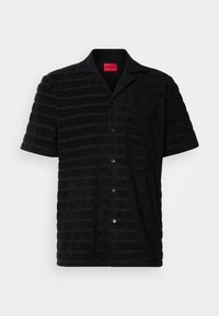 Chemise noire à manches courtes avec boutons, rayures horizontales discrètes, col pointu, poche poitrine et étiquette rouge "HUGO" à l'intérieur du col.