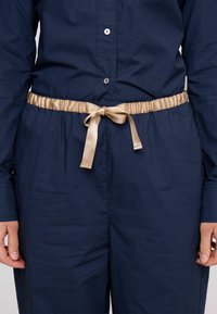 Tengerészkék ruhadarab sima textúrával, bézs szatén szalaggal a deréknál megkötve. Gombok futnak végig az elején.