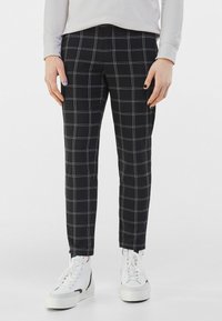 Černé kárované kalhoty s bílými a světle šedými proužky, úzkého střihu, s hladkou texturou. Kombinovány s bílými vysokými teniskami.