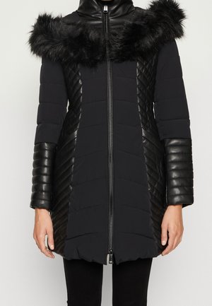 Abrigo largo negro acolchado con cuello de piel, paneles laterales con textura de cuero y mangas acolchadas de cuero, cerrado con cremallera en una persona de pie.