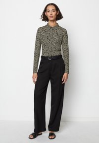 Maglietta a maniche lunghe, aderente, in stampa leopardata nera e beige, abbinata a pantaloni neri a vita alta e gamba larga, e sandali neri senza chiusura.