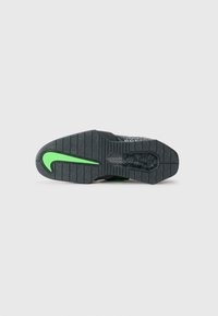 Sko sål med en struktureret sort gummioverflade, der har et fremtrædende grønt Nike-swoosh og et detaljeret dækmønster for god traction.