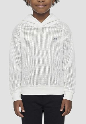 Dijete odjeveno u bijelu mrežastu hoodicu s malim kvadratnim logom na prsima, u kombinaciji s crnim hlačama, stoji ispred jednobojne pozadine.