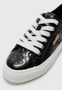 Svarta vadderade sneakers med glansig finish, som har vita snören och guld-logotyp. Sålen har ett strukturerat vitt mönster.