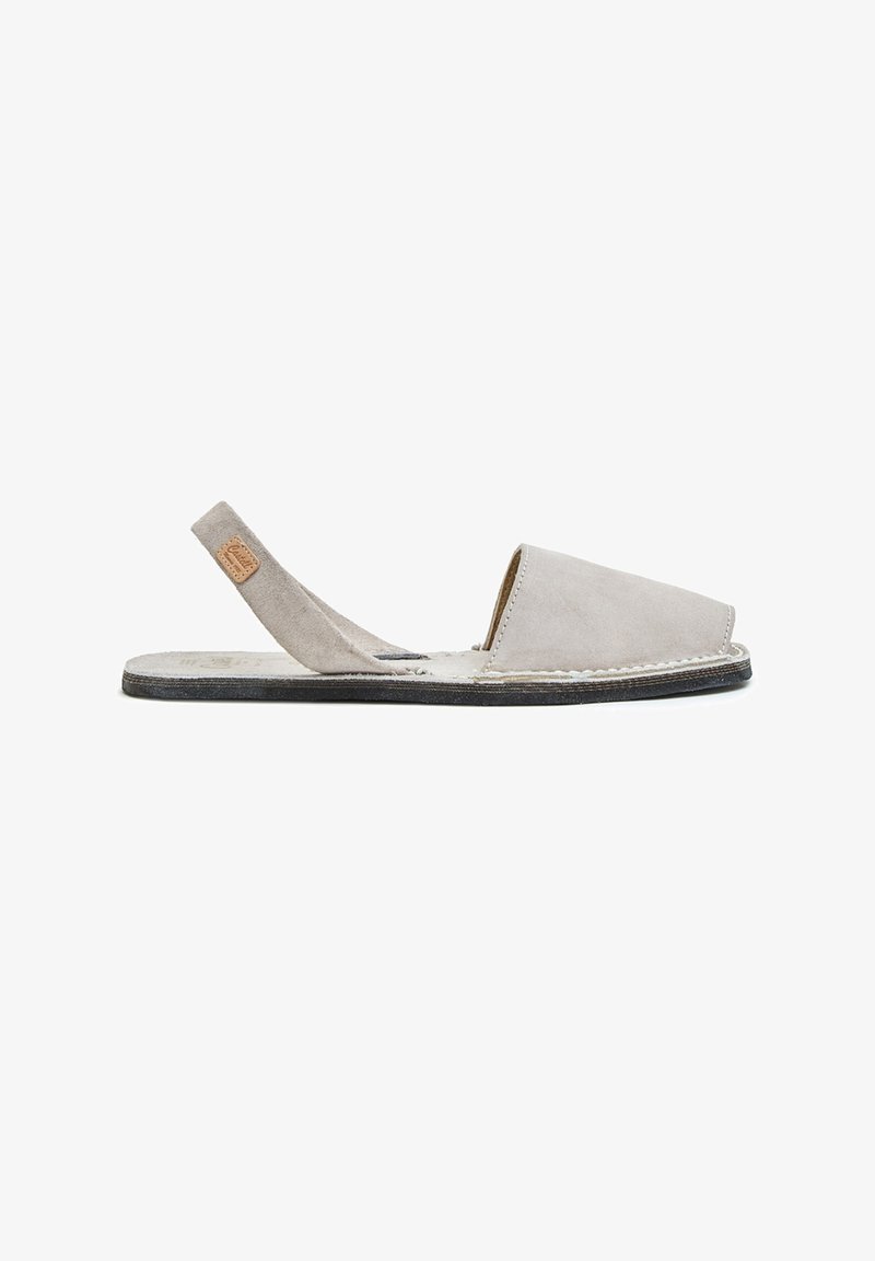 Sandalia slingback de ante gris claro con puntera cerrada, suela plana negra y detalles cosidos sobre un fondo blanco.