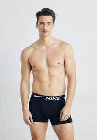 Svarte Nike boxershorts med hvit logo på midjebåndet. Modellen har en muskuløs bygning og er uten skjorte, noe som viser frem undertøyet.