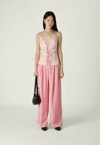 Haut sans manches rose clair avec un devant en dentelle, associé à un pantalon ample rose à larges jambes. Accessoirisé avec un sac à main noir et des chaussures foncées.