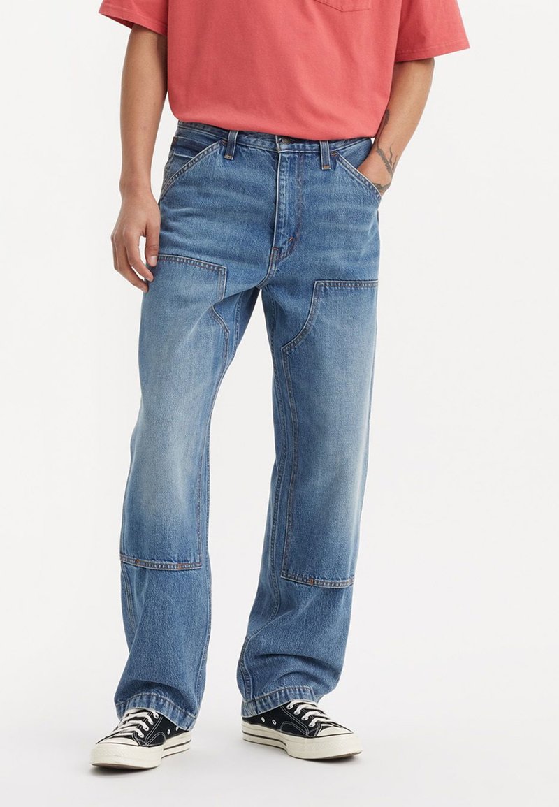 Lyseblå denimjeans med løs passform, synlige sømdetaljer og to frontlommer. Kombinert med svarte sneakers.