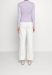 Lila geripptes Langarmshirt kombiniert mit weißen Schlaghosen und silbernen Absatzsandalen, von hinten betrachtet. Sauberes und minimales Design.
