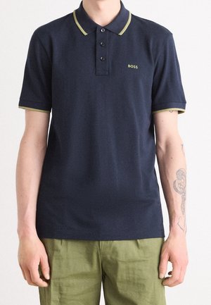 Polo bleu marine en coton avec col et accents de manches verts. Comprend trois boutons et un petit logo sur le côté gauche de la poitrine.