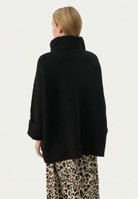 Zwarte oversized trui met een hoge rolkraag, ribbeltextuur en ingezette schouders, gecombineerd met een broek met panterprint.