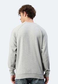 Felpa grigia in cotone con collo a giro e maniche lunghe raglan, caratterizzata da un tessuto testurizzato e una vestibilità rilassata. Dettagli di cucitura significativi.