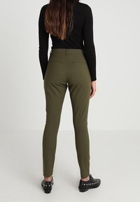 Olivgröna skräddarsydda byxor med sidofickor, slät textur och medelhög midja. Bärs med svarta ankelsboots med silvernitar.