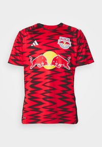 Maglietta da calcio rossa con motivi a zigzag neri, caratterizzata da un cerchio giallo e il logo di due tori rossi. Realizzata in tessuto traspirante, maniche corte.