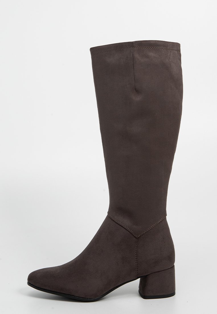Brauner knöchelhoher Stiefel aus Wildleder mit niedrigem Blockabsatz und spitzem Zehenbereich, vor einem schlichten weißen Hintergrund präsentiert.