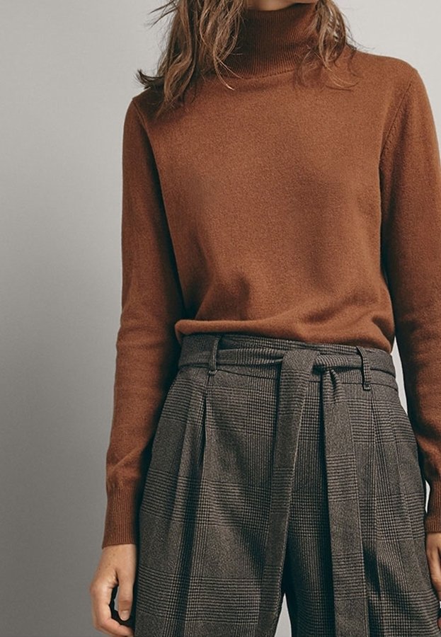 Femme portant un pull à col roulé marron rentré dans un pantalon gris à carreaux taille haute avec une ceinture nouée.