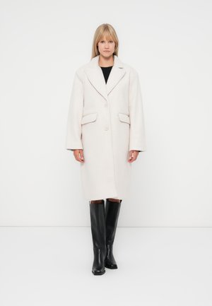 Light beige wool blend coat with a soft texture, notched lapel, two front pockets, and two buttons, paired with black knee-high boots.