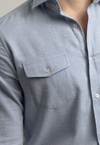 Camisa azul claro de botones hecha de tela suave con un acabado texturizado. Cuenta con un bolsillo en el pecho y botones redondos para el cierre.