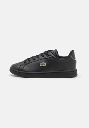 Baskets basses noires avec lacets noirs et petit logo crocodile vert sur le côté, présentées sur fond blanc.