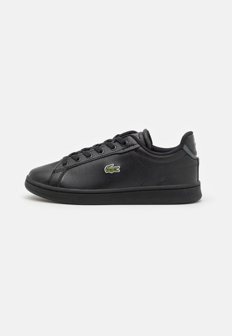 Baskets basses noires avec lacets noirs et petit logo crocodile vert sur le côté, présentées sur fond blanc.