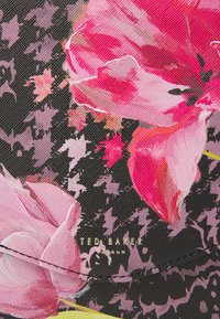 Tissu à motif floral avec de grandes fleurs roses sur un fond noir. Comprend le logo doré "Ted Baker" près du bas.